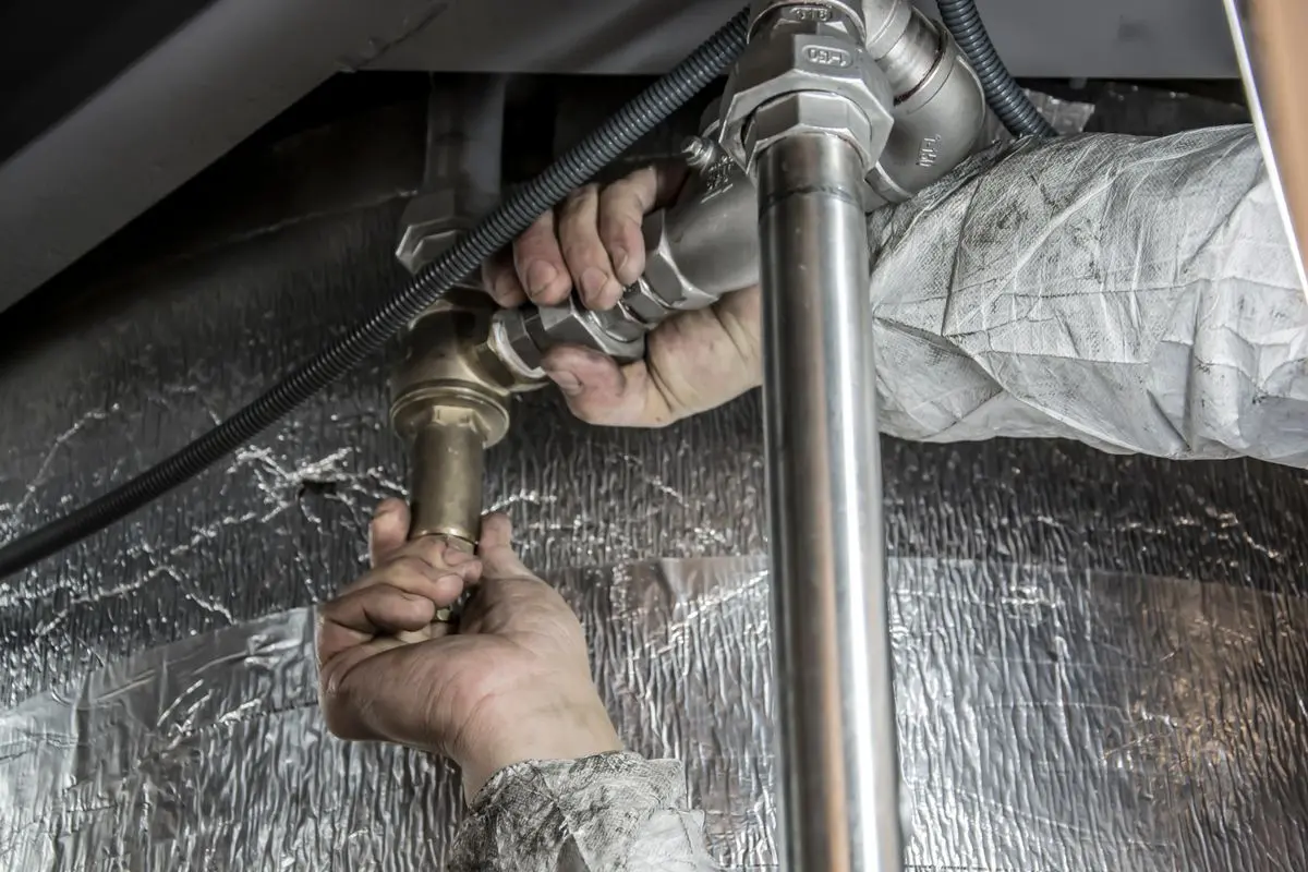 Monteur arbeitet an einem Siphon und der Abflussleitung unter einem Waschbecken